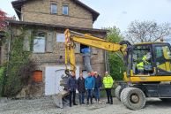 Fünf Männer stehen vor einem alten Haus, ein weiterer Mann sitzt in einem Bagger. Aus einem Fenster des Hauses hängt ein Schrotttrichter. Bei den Personen handelt es sich um Bürgermeister Ulrich Berger, Martin Westermeier (Fachbereichsleiter Stadtentwicklung), Sam Seyfzadeh (Klimaschutz- und Mobilitätsmanager), erster stellvertretender Bürgermeister Norbert Menke, Michael Horstknepper (Fachdienstleiter Gebäudemanagement) und Michael Stelbrink (Bauleiter von Stelbrink Tief- und Straßenbau GmbH)