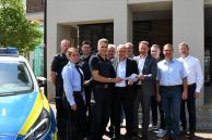 Das Foto zeigt eine Gruppe aus Menschen, die vor den neuen Räumlichkeiten der Polizei im Rathaus der Stadt Salzkotten stehen. Einige von Ihnen tragen eine Polizeiuniform. Links neben ihnen steht ein Polizeifahrzeug.