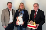 Das Foto zeigt drei Personen vor einem weißen Hintergrund. Links steht Bürgermeister Ulrich Berger, daneben, in der Mitte, Doris Fecke. Sie hält die Urkunde zur Ernennung als neue Ortsheimatpflegerin in der Hand. Rechts neben ihr steht Norbert Schulte, ihr Vorgänger. Er hält einen Präsentkorb in den Händen