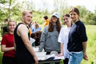 Es ist eine Gruppe aus jungen Menschen zu sehen. Sie stehen im Grünen um einen Tisch herum, auf dem Forschungsmaterial und viele Zettel liegen.