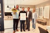 Das Foto zeigt vier Personen, die in einem Optikerfachgeschäft stehen. Die Stadt Salzkotten mit Bürgermeister Ulrich Berger, Stefanie Klenke von Salzkotten Marketing e. V. und Dirk Witulski vom Verkehrsverein Salzkotten überreichen dem Inhaber Marcel Abu-Baker eine Urkunde und einen Blumenstrauß zur Neueröffnung.