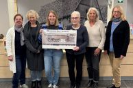Das Foto zeigt sechs Frauen, die nebeneinander im Foyer der Stadtbibliothek Salzkotten stehen. Zwei von ihnen halten den Spendenscheck über 1550 Euro in den Händen. Es handelt sich um die Scheckübergabe der Spenden, die beim Benefizabend mit dem Kabarett Radau in der Stadtbibliothek gesammelt wurden, an die Speisenkammer Salzkotten.