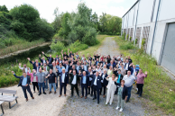 Das Foto zeigt eine große Gruppe Menschen, die auf einem Weg vor einem Gebäude stehen und in die Kamera winken