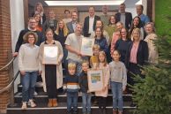 Alle Preisträger und der Bürgermeister Ulrich Berger, der Klimaschutz- und Mobilitätsmanager Sam Seyfzadeh und Fabian Wälter von Westenergie stehen als Gruppe auf der Treppe, die zum Ratssaal führt, im Rathaus der Stadt Salzkotten. Die Preisträger halten stolz ihre Urkunden in Richtung Kamera.