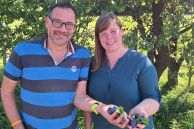 Ein Mann und eine Frau stehen vor einem Pflaumenbaum. Sie halten frischgepflückte Pflaumen in den Händen