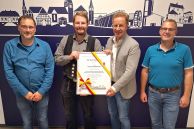 Vier Männer stehen nebeneinander vor einer LED-Wall, die die Silhouette der Stadt Salzkotten abbildet. Die Mann rechts in der Mitte überreicht dem Mann links neben ihm eine Urkunde.