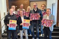 Acht Personen stehen auf der Treppe, die zum Ratssaal führt, im Rathaus der Stadt Salzkotten. Sie halten den Adventskalender in der Hand.