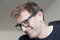 Autor Andreas Henke sitzt an einem Schreibtisch und schaut einen Monitor