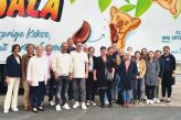 Im Hintergrund steht ein großer LKW mit dem Aufdruck von den Koala-Süßigkeiten, die von KuchenMeister produziert werden. Vor dem LKW steht eine Menschengruppe aus 20 Personen, die alle in Richtung der Kamera schauen.