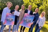 Lukas Michalski (Stadt Salzkotten), Heike Menke (Leitung Familienzentrum KiTa Regenbogen), Lukas Droste (Warsteiner Brauerei), Martin Herbst (Volksbank Büren-Salzkotten), Bürgermeister Ulrich Berger und Stefanie Klenke (Stadt Salzkotten) stehen vor der Heder im Franz-Kleine-Park und halten die Plakate zum Film in der Hand.