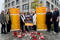 Vor dem Delbrücker Rathaus stehen zehn Frauen. Zwischen ihnen stehen zwei gelbe Roll-ups, auf denen &quot;#keinegewalt&quot; steht. Vor den Frauen stehen rote Schuhe und Grabkerzen.