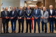 Sieben Vertreter aus Kirche, Politik und Stadtverwaltung stehen nebeneinander im Foyer des neuen Rathauses. Vor ihnen ist ein rotes Band mit einer Schleife in der Mitte gespannt. Jeder von ihnen hält eine Schere in der Hand, die sie bereit zum Durchschneiden des Bandes an das Band halten.