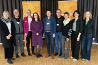 Sechs Frauen und drei Männer stehen nebeneinander auf einer Bühne mit hellem Parkettboden. Hinter ihnen stehen zwei orangefarbene Roll-ups mit der Aufschrift "#keineGewalt". Den Hintergrund bildet ein grauer Vorhang, der bis zum Boden reicht. Die neun Personen sind die Gleichstellungsbeauftragten aus den Kommunen, die zum Kreis Paderborn gehören.