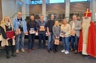 Die Verantwortlichen aus dem Fachbereich Bildung &amp; Soziales stehen zusammen mit Bürgermeister Ulrich Berger und dem Nikolaus im Ratssaal der Stadt Salzkotten. Im Hintergrund stehen viele gepackte Geschenktüten.