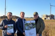 Christian Hübner (Stadt Salzkotten), Bürgermeister Ulrich und der stellv. Bürgermeister Norbert Menke stehen im Baugebiet Osterfelde auf einem Weg, vor zwei Krähnen und halten das Expose in der Hand.