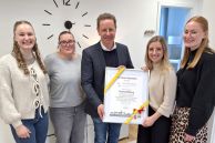 Fünf Personen steht im Eingangsbereich einer Praxis. In der Mitte steht Bürgermeister Ulrich Berger, der den vier Mitarbeiterinnen der Logopädiepraxis eine Eröffnungsurkunde der Stadt Salzkotten überreicht.