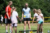 Spielende Kinder und Erwachsene auf einer Wiese vor einem Waldstück Spikeball.