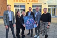 Die Veranstalter der SAME GAME stehen vor der Mensa der Gesamtschule Salzkotten. Sie halten ein Plakat für die Veranstaltung hoch.