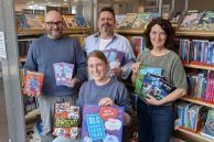 Foto (Gernot Hüsgen): Das Team der Stadtbibliothek Salzkotten freut sich auf viele lesebegeisterte Kinder und Jugendliche beim Sommerleseclub 2026. Im Bild (v. l.): Nicos Sprenger, Hartmut Hilleke, Inge Adrian und Maike Sprenger (vorne) stehen vor einem Bücherregal in der Stadtbibliothek und halten Bücher und Plakate in der Hand.