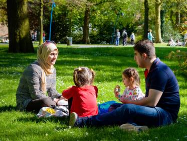 Familie mit Migrationshintergrund sitzt auf einer Wiese und picknickt