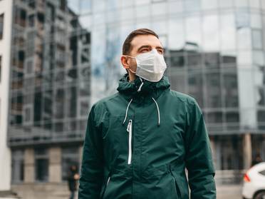 Mann mit Maske vor einem Firmengebäude